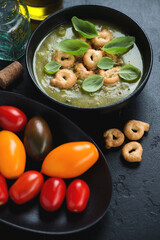 Bowl of vegetable soup with green peas, spinach, leek and tarallini, vertical shot on a black stone background