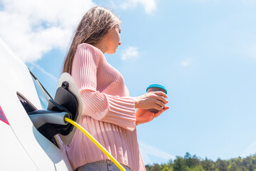 Woman taking a coffee break while charging her electric car
