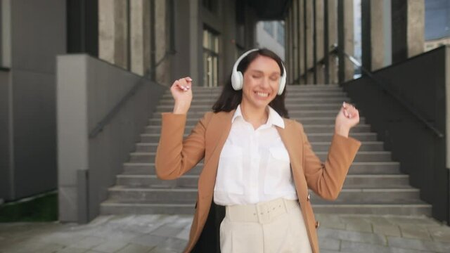 Happy businesswoman in headphones dancing and smiling walking along modern office centre. Success. Motivation. High quality 4k footage