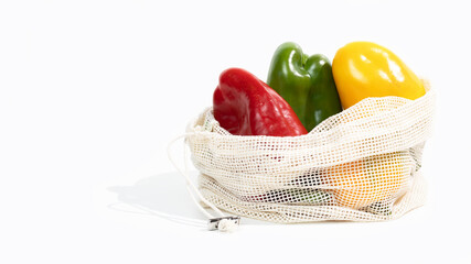 Ripe yellow, green and red bell pepper lies in a fabric net string bag. Shopping local seasonal vegetables.