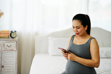 pregnant woman using mobile phone to check some news and search the knowledge about baby care in bed room.