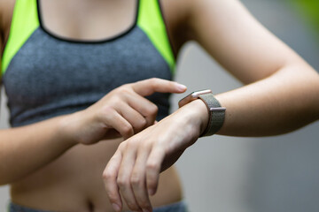 Close up a woman looking at a smart watch while jogging in the park.