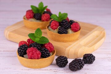 Tartlets with berries and vanilla cream are decorated with a mint leaf.
