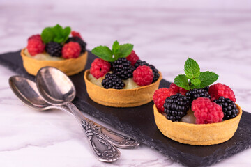 Tartlets with raspberries and blackberries and tender cream on a black slate board for serving.