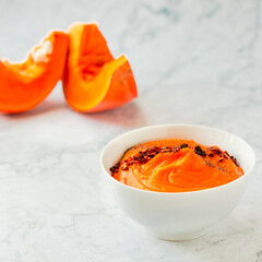 Pumpkin and carrot soup with chili flakes pepper on a white marble background. Copy space. Autumn comfort food concept