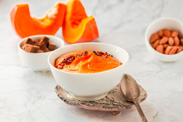 Bowl of tasty pumpkin soup ith chili flakes pepper, nuts and croutons.Space for text on marble table
