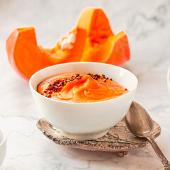 Bowl of tasty pumpkin soup ith chili flakes pepper, nuts and croutons.Space for text on marble table