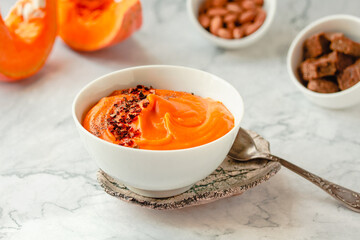 Pumpkin soup and organic pumpkins on marble table. Seasonal autumn food - Spicy pumpkin and carrot soup