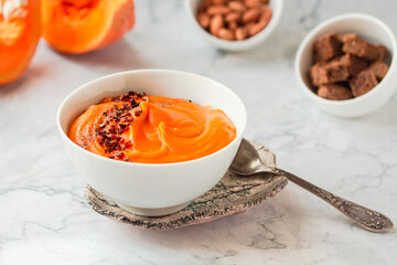 Pumpkin soup and organic pumpkins on marble table. Seasonal autumn food - Spicy pumpkin and carrot soup