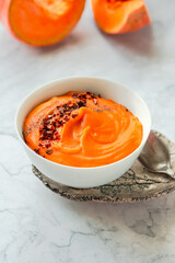Tasty appetizing pumpkin creamy soup decorated with chili flakes pepper served in white bowl on marble background. Selective focus