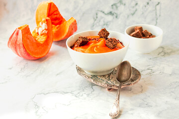 Roasted pumpkin and carrot soup with black and chili flakes pepper, rye crispy toast on marble background.Traditional fall and winter dishes