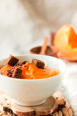 Bowl of tasty pumpkin soup with chili flakes pepper and rye crispy toast croutons on autumn comfort background. Traditional fall and winter dishes concept