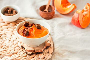 Bowl of tasty pumpkin soup with chili flakes pepper and rye crispy toast croutons on autumn comfort background. Traditional fall and winter dishes concept