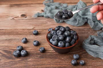 A person's hand holding a spoon full of blueberries picked from a bowl