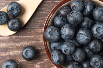 Set of blueberries in a bowl on a wooden table and a wooden spoon with 3 berries. Macrophotography