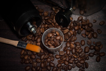 top view of roasted coffee beans flow down from manual coffee grinder with orange brush, soft focus