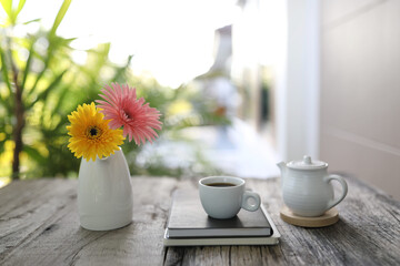 White coffee cup and tea pot with notebook and gerbera flowers