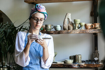 Woman on the background of a shelf in a ceramic workshop makes dishes, daylight, half-length portrait