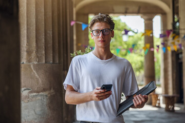 A man with a smartphone in his hands looks at the camera. Business young man wearing glasses with smartphone