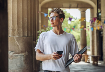 Young handsome man goes to the university and writes a message in the smartphone. A modern man does business in a smartphone.