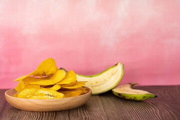 Banana chip or locally known as kerepek pisang in wooden plate with raw halved banana. Selective...