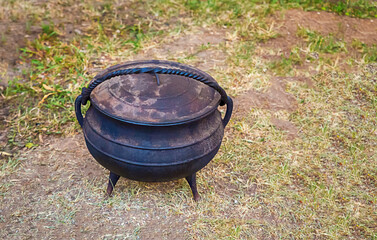 black cast iron pot stands on the background of the earth, cooking in nature