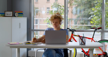 Fototapeta na wymiar Portrait of teen boy in headphones doing homework on laptop at home