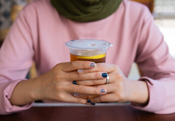 a cup of lemon tea ice is on the table. a girl holds a tasty beverage in her hand. a kind of enjoying leisure time.