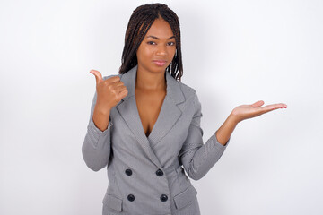 Happy cheerful Young african american business woman with braids over white wall showing thumb up and pointing with the other hand. I recommend this.