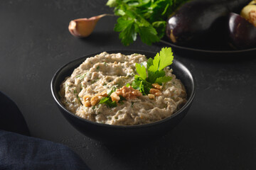 Baba ganoush Asian cuisine appetizer made from baked eggplant with parsley, garlic and olive oil on black table. Close up.