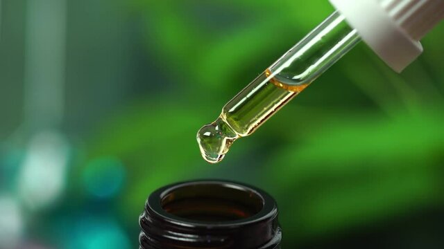 CBD Hemp oil, Hand holding droplet of Cannabis oil against blurry beaker background. Alternative Medicine. droplet dosing a biological and ecological hemp plant herbal pharmaceutical cbd oil.	