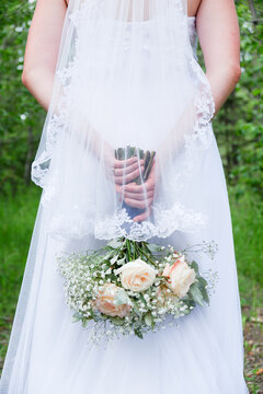Bride holding a bouquet of roses standing near green trees