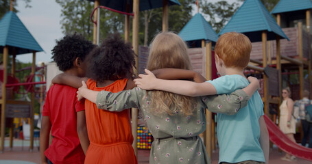 Back view of diverse preschool kids embrace on playground