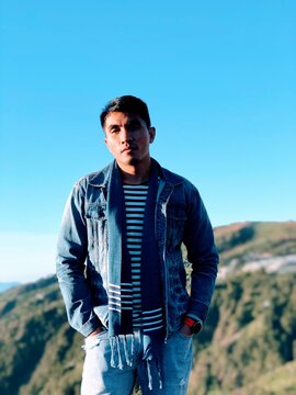 Man in blue scarf and denim jacket standing near mountain
