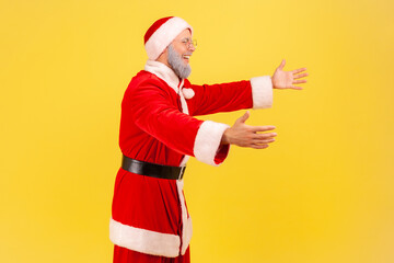 Side view of egoistic elderly man with gray beard wearing santa claus costume standing with raised...