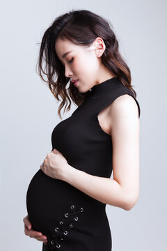 Side view of a woman standing and touching pregnancy bump