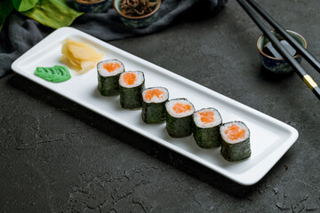 Maki roll with salmon on white plate on black stone table