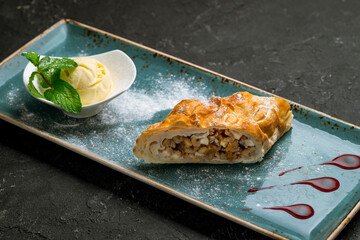 Apple strudel with ice cream on plate on black stone table