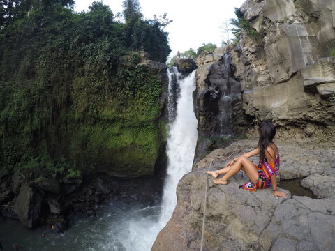 Woman sitting on rock and looking at waterfall nearby
