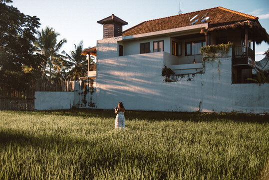 Woman Standing On Green Grass Beside A House And Trees