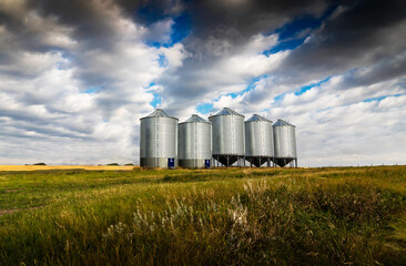 Fototapeta na wymiar Grain silos standing tall on a harvested wheat field under a dramatic sky in Rockyview County Alberta Canada