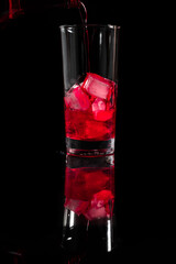 Pouring red thick juice on the top of the ice into the glass against complete dark background. copy space. Pour alcohol,