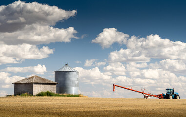 A farm tractor and auger filling a grain silo on a prairie wheat field in Rockyview County Alberta Canada.