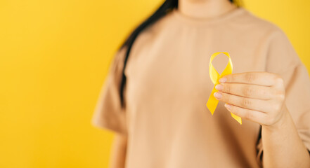 a woman holding a yellow gold ribbon in her hand on a yellow background, Bone cancer, awareness of childhood cancer, yellow September, the concept of World Suicide Prevention Day - obrazy, fototapety, plakaty