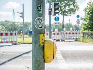 Ein Ampelpfeiler mit Aufklebern im Vordergrund, Schilder und eine Baustelle im Hintergrund