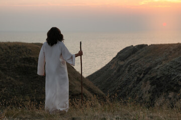 Fototapeta premium Jesus Christ with stick on hills at sunset, back view. Space for text