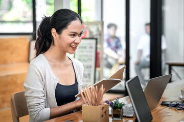 Image of a happy young Asian woman holding a notebook stay focused on working at the office.