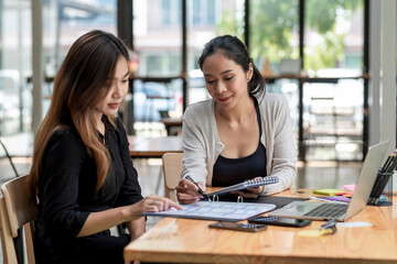 Team of young Asian businesswoman sitting at work brainstorming  analyze holding a notebook pen pointing at the document the laptop is placed on the office desk.