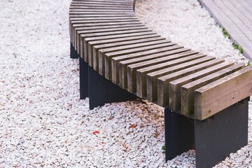 Curved modern wooden bench at public park or street with blurred white stones path on...