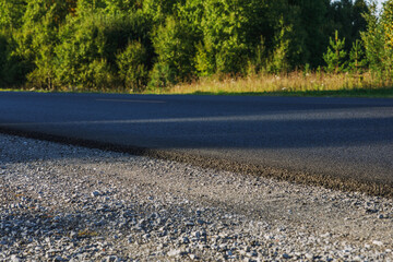 A track with fresh asphalt and a yellow dividing strip. Green grass grows on the side of the road. Summer landscape on a warm sunny day.